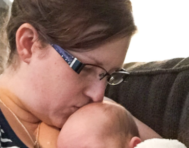 Mom kissing newborn's head grieving a newborn experience she didn't have